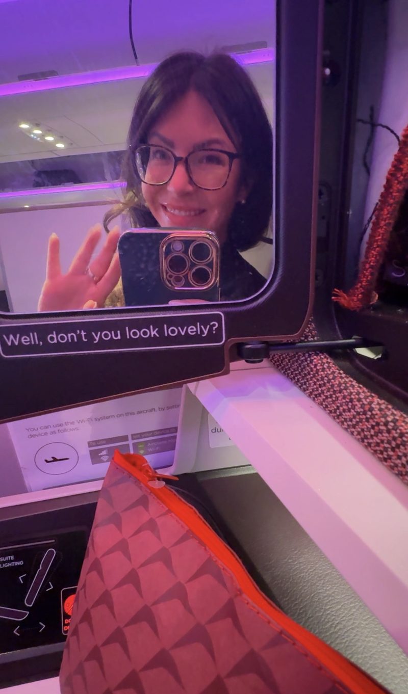 Liane waving in the Upper Class suite mirror that reads Well, don't you look lovely?